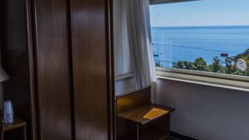 A room with a view of the sea, a wooden wardrobe, a small wooden bench, and a tiled floor.