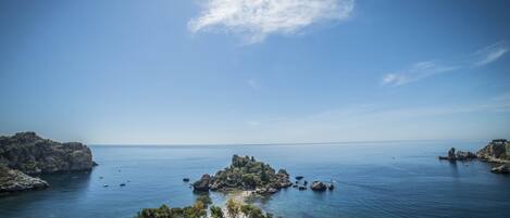A coastal landscape with rocky outcrops, clear blue water, and a small island with a building.