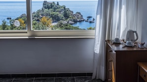 Una habitación de hotel con un ventanal grande que ofrece vistas a una isla rocosa y al mar.