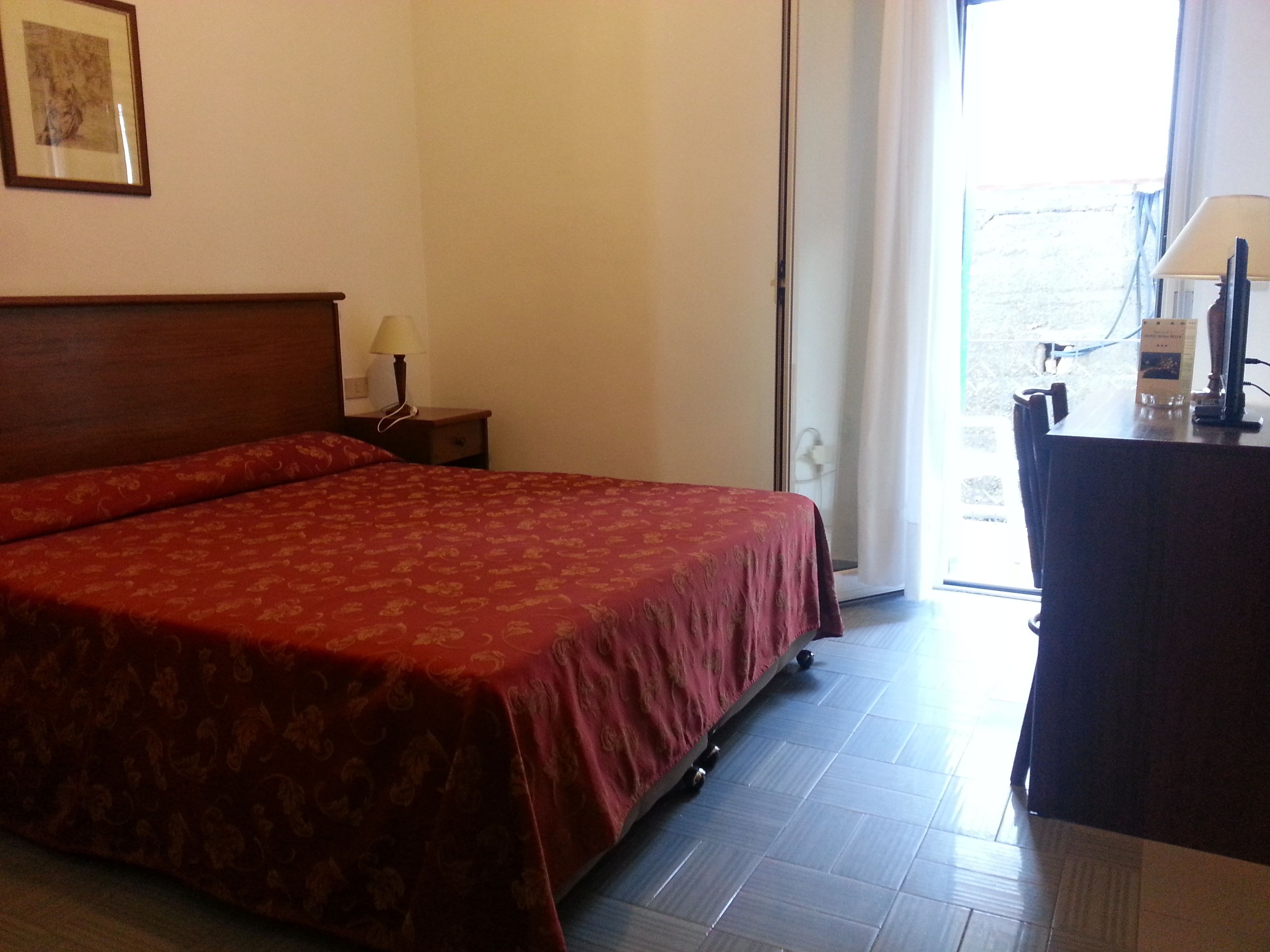 Une chambre d’hôtel avec un grand lit, un bureau, une chaise, une lampe et une fenêtre avec des rideaux.