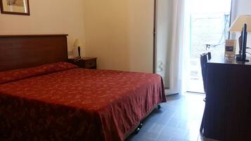 Une chambre d’hôtel avec un grand lit, un bureau, une chaise, une lampe et une fenêtre avec des rideaux.