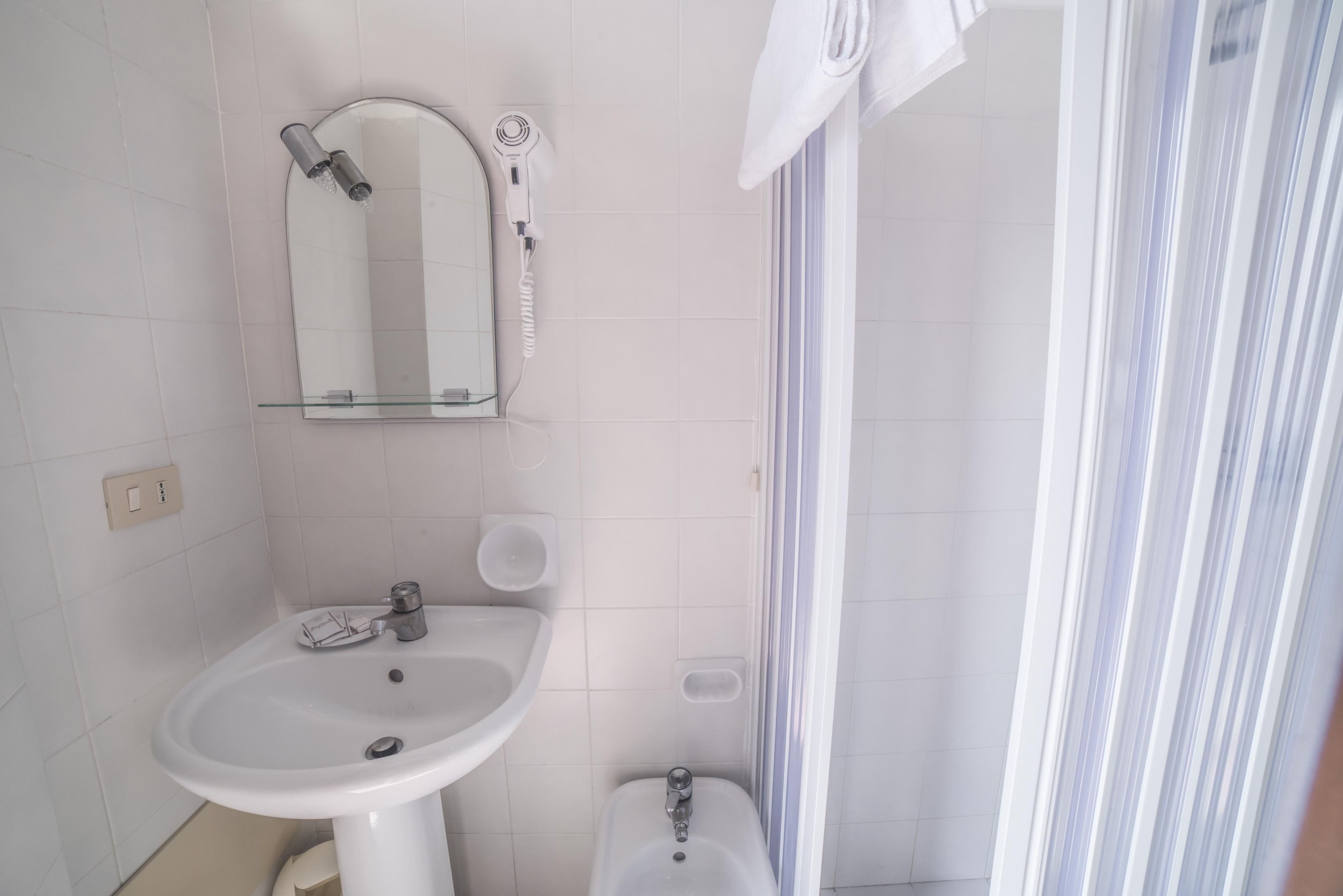 Un baño con lavamanos pedestal blanco, espejo, secador de pelo portátil y cortina de ducha.