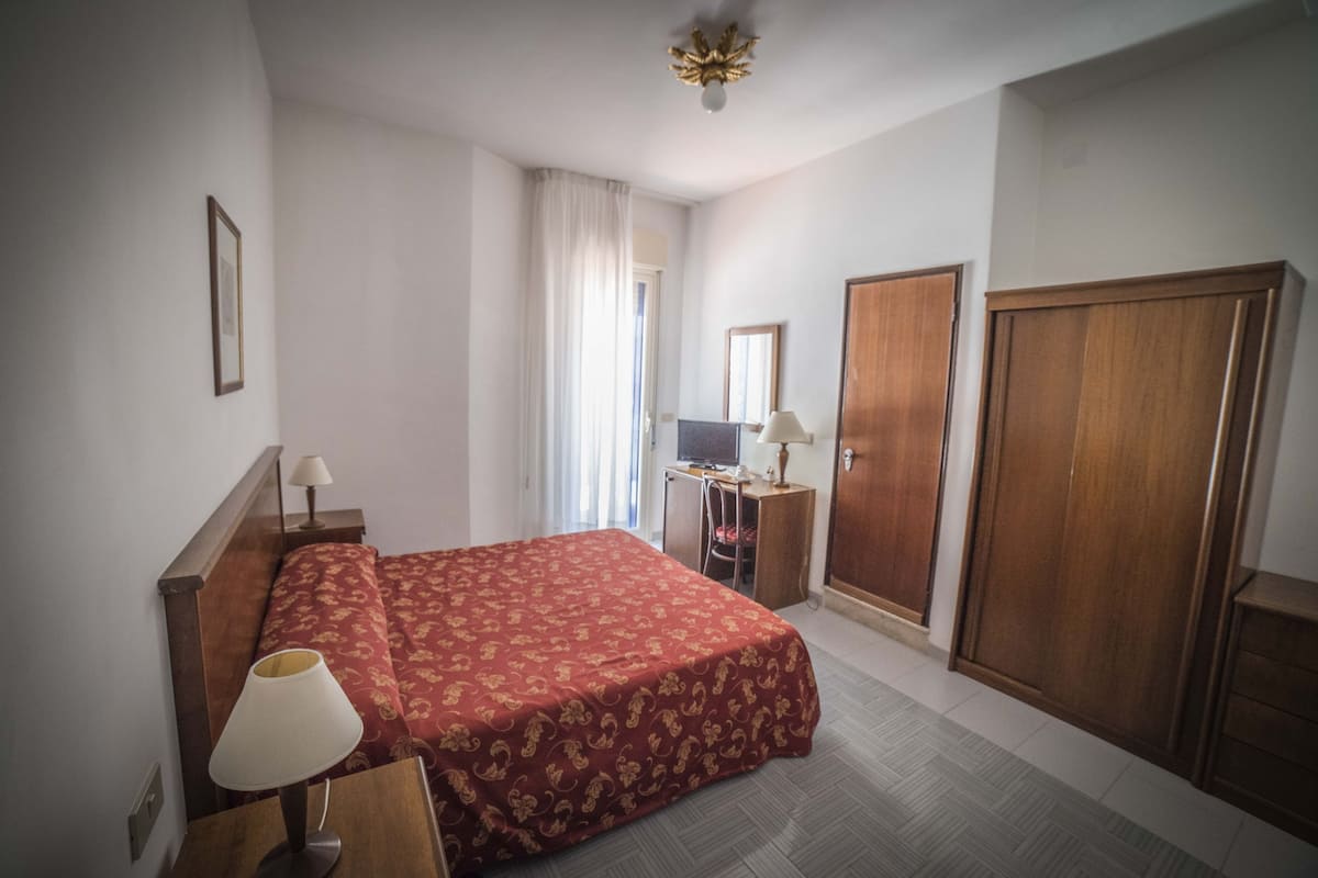 A hotel room with a bed, a desk, a chair, a wardrobe, and a television.