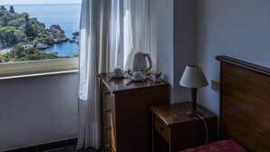 Habitación de hotel con cama, escritorio, lámpara y vista al mar.