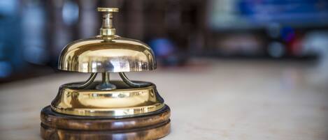 A brass bell on a wooden base, likely used for signaling room service or guest requests.