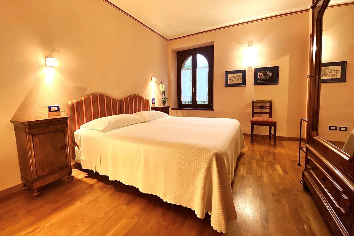 A hotel room with a large bed, wooden floor, a nightstand, a chair, and a mirror.