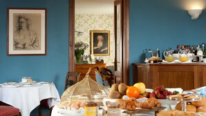 A breakfast setting with a table set for two, featuring eggs, pastries, and fruit.