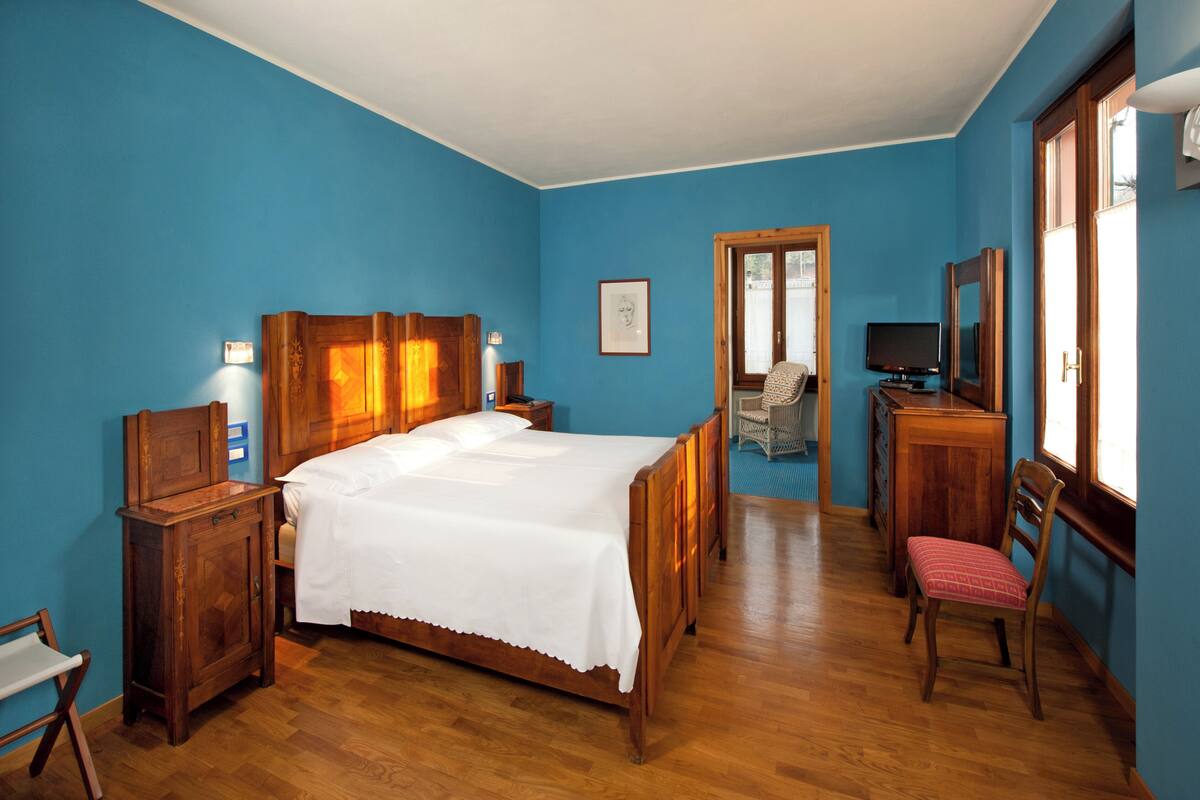 A bedroom with a wooden bed, a desk, a chair, a television, and a window.