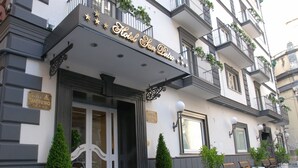 Ein Hotel mit einer klassischen Fassade, einem markanten Eingang mit Glastür und einem Balkon mit Blumentöpfen.