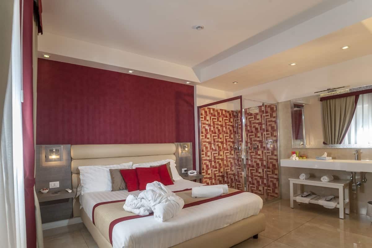 A hotel room with a large bed, a shower enclosure, a vanity with a mirror, and a bedside table with a lamp.