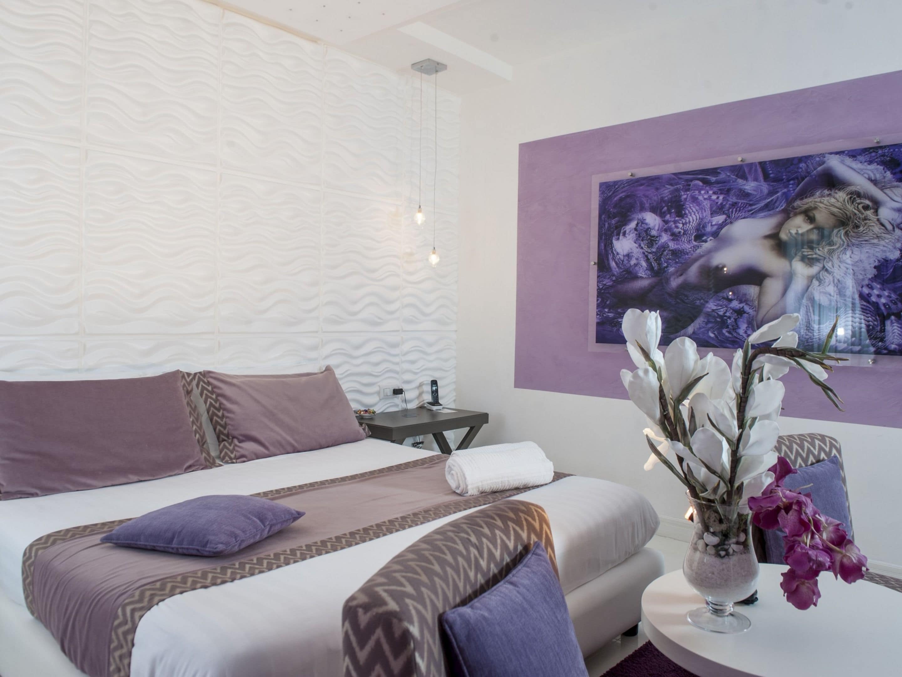 A modern bedroom with a bed, a sofa, a nightstand, and a wall-mounted painting.