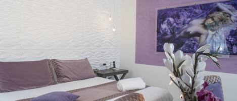 A modern bedroom with a bed, a sofa, a nightstand, and a wall-mounted painting.