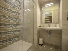 Une salle de bain moderne avec une douche à parois de verre, un mur recouvert de carreaux de marbre, un lavabo avec un miroir et des articles de toilette disposés sur le comptoir.