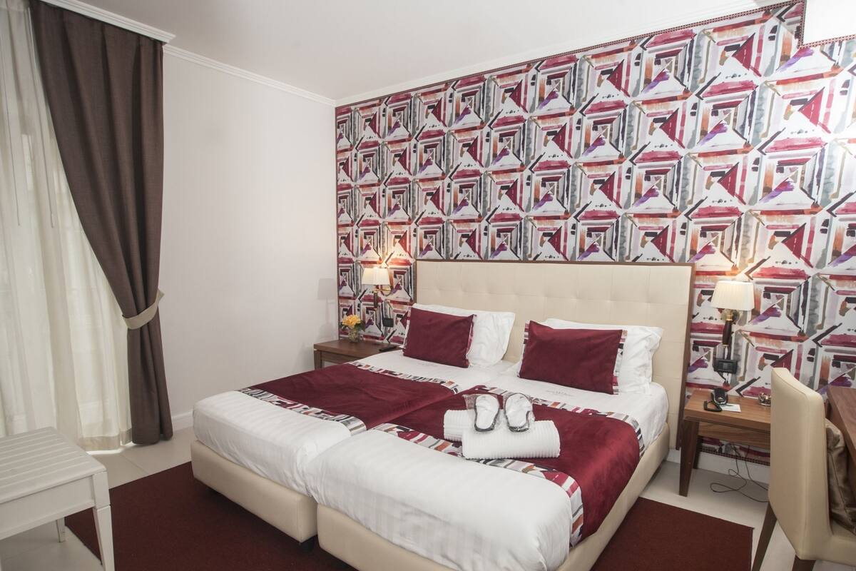 A double bed with a red and white patterned headboard, a bedside table with a lamp, and a chair.