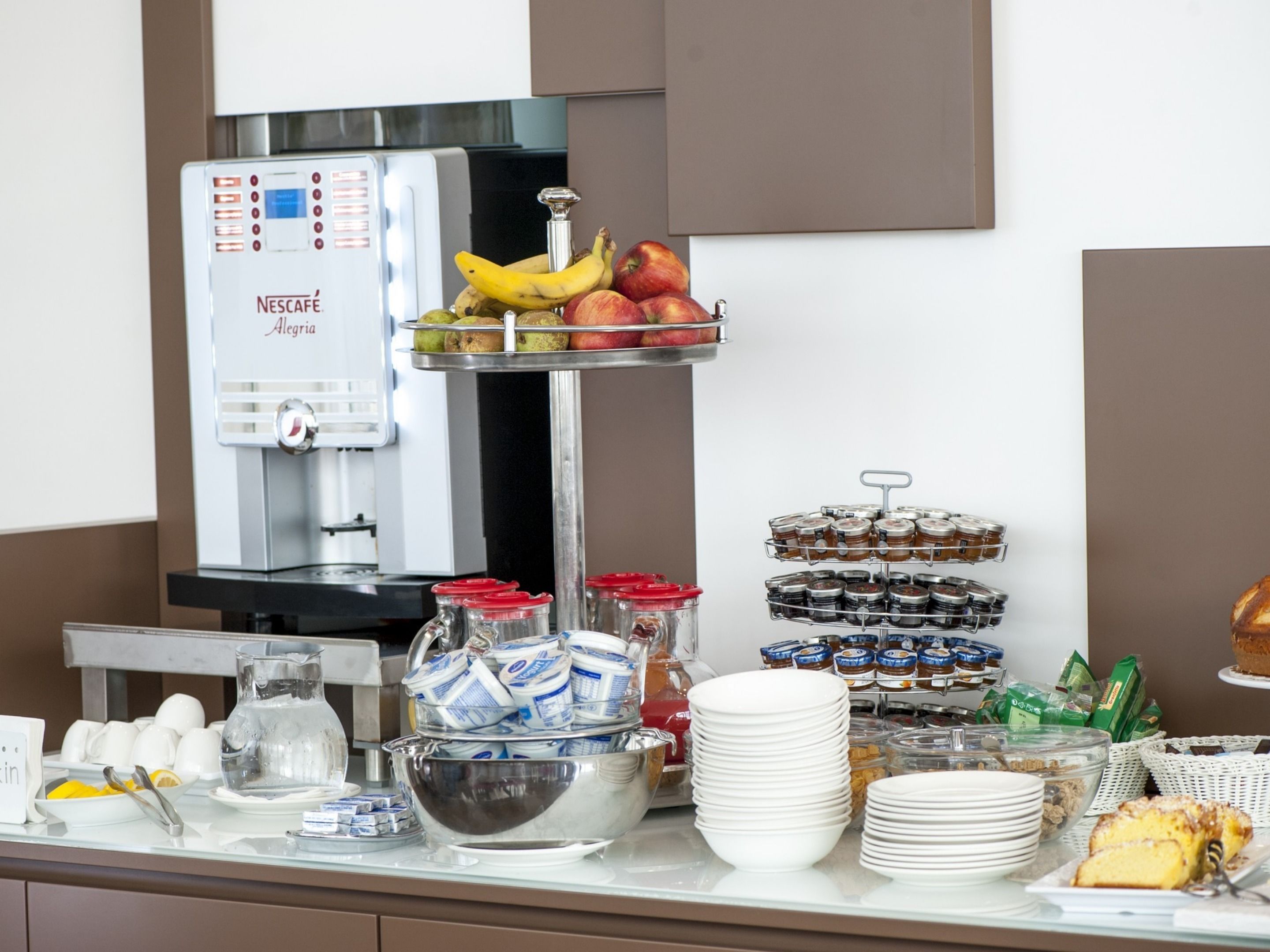 A buffet setup with a Nescafé coffee machine, fruits, condiments, and various food items.
