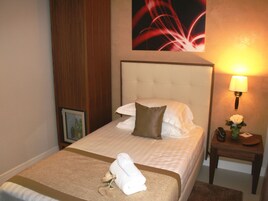 A hotel room with a neatly made bed, a bedside lamp, a small table with a vase of flowers, and a framed picture on the nightstand.