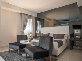A modern hotel room with a large bed, two armchairs, a small round table, and a TV.