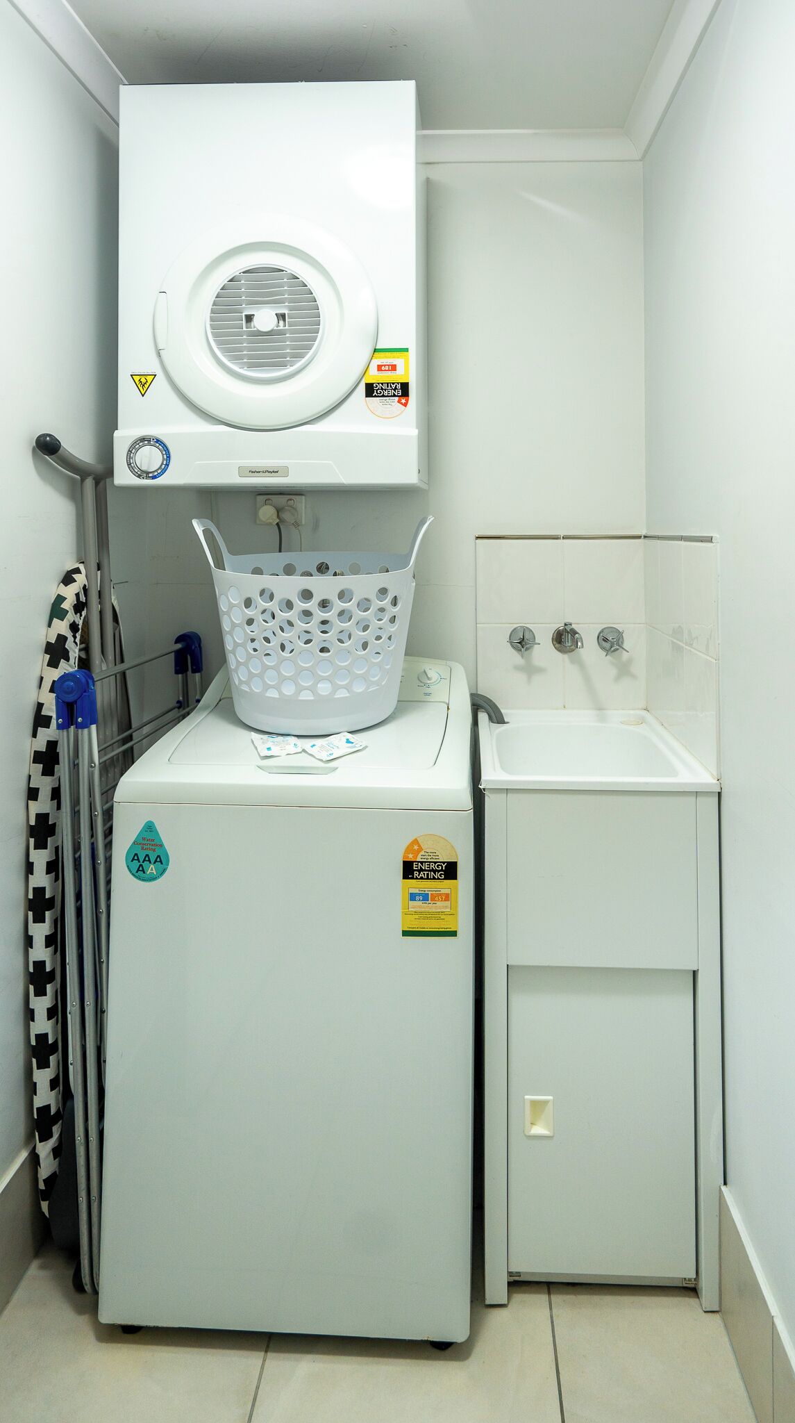 A compact laundry room with a front-loading washer and dryer, a small sink, and a metal rack.