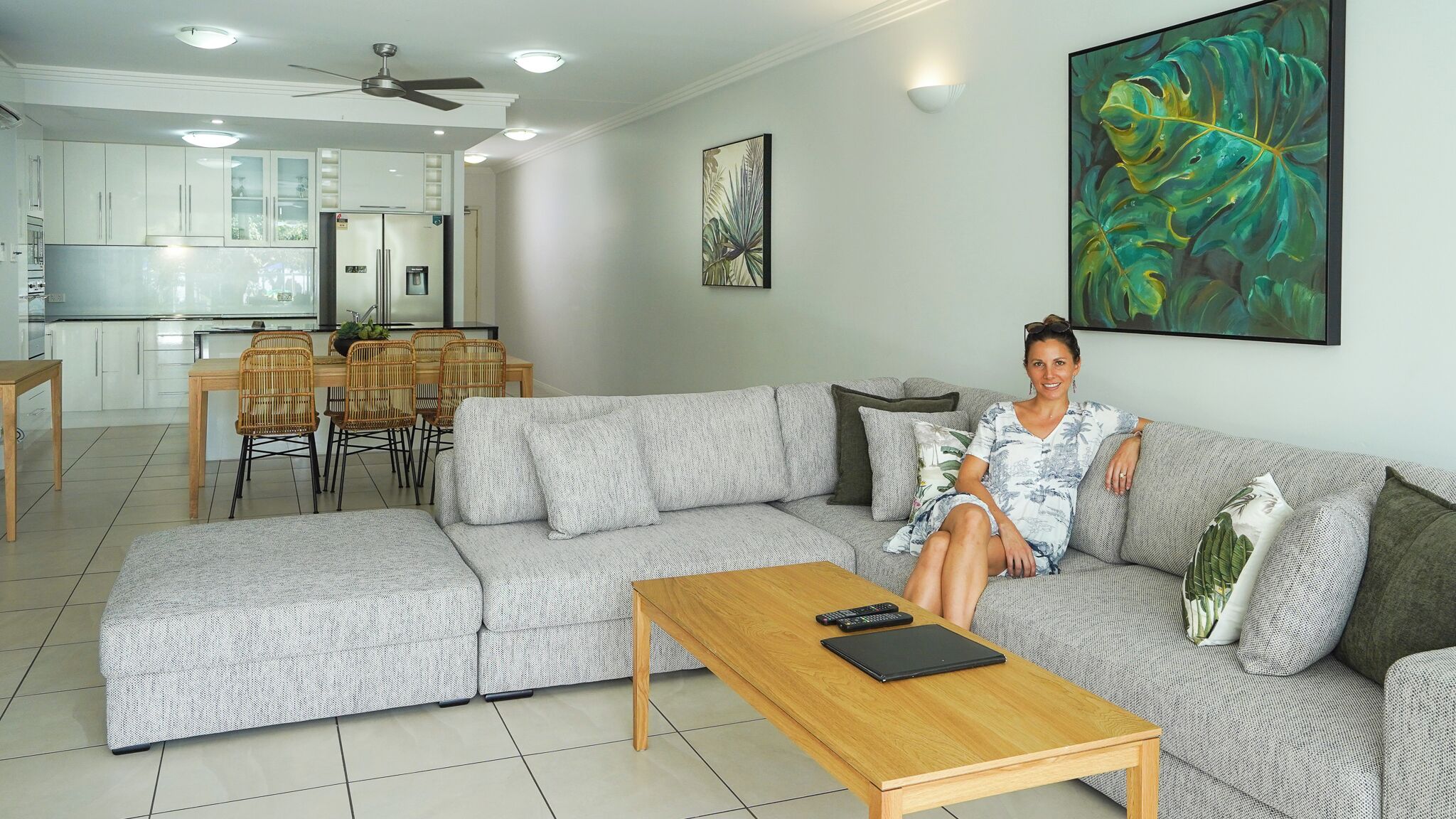 A modern living room with a grey sectional sofa, a wooden coffee table, and a dining area with wicker chairs.