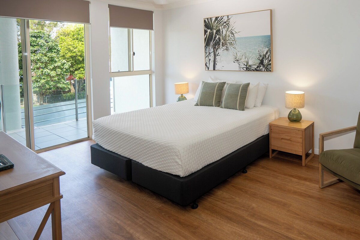 A bedroom with a bed, bedside tables, a chair, and a window with a view of greenery.
