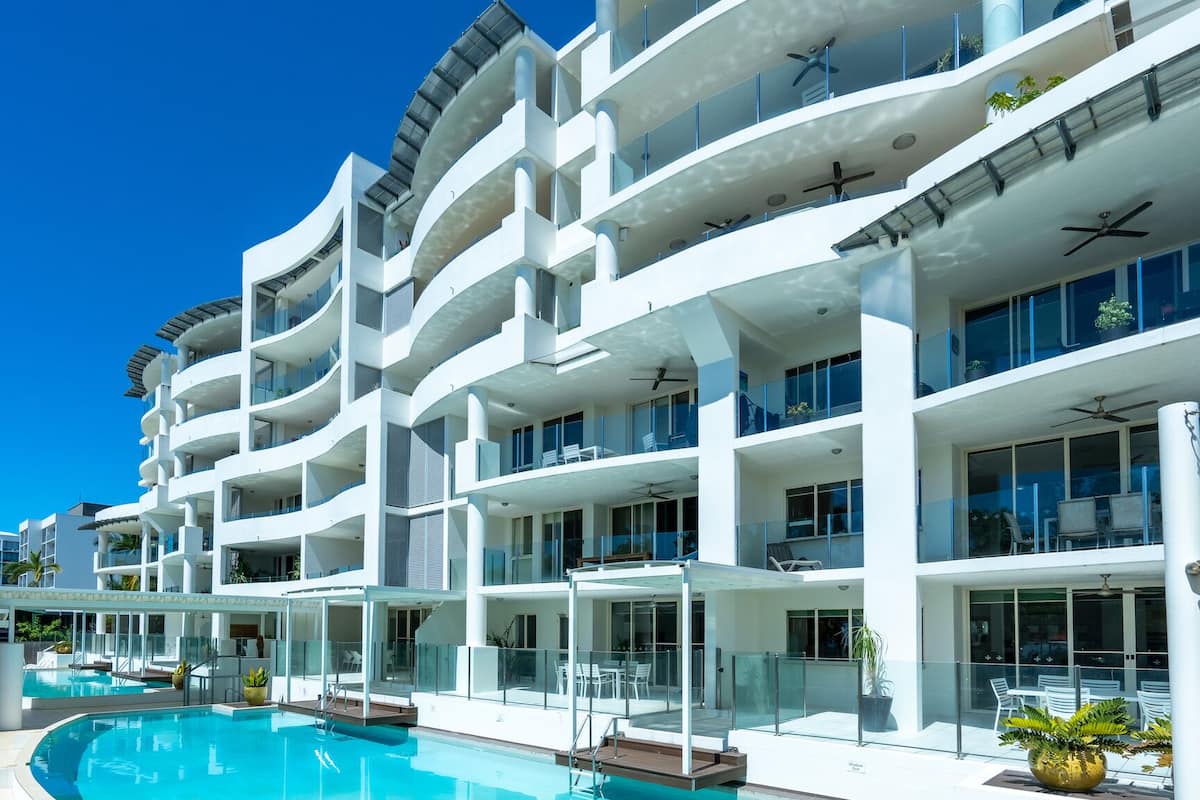 A modern hotel with multiple balconies, a swimming pool, and outdoor seating areas.