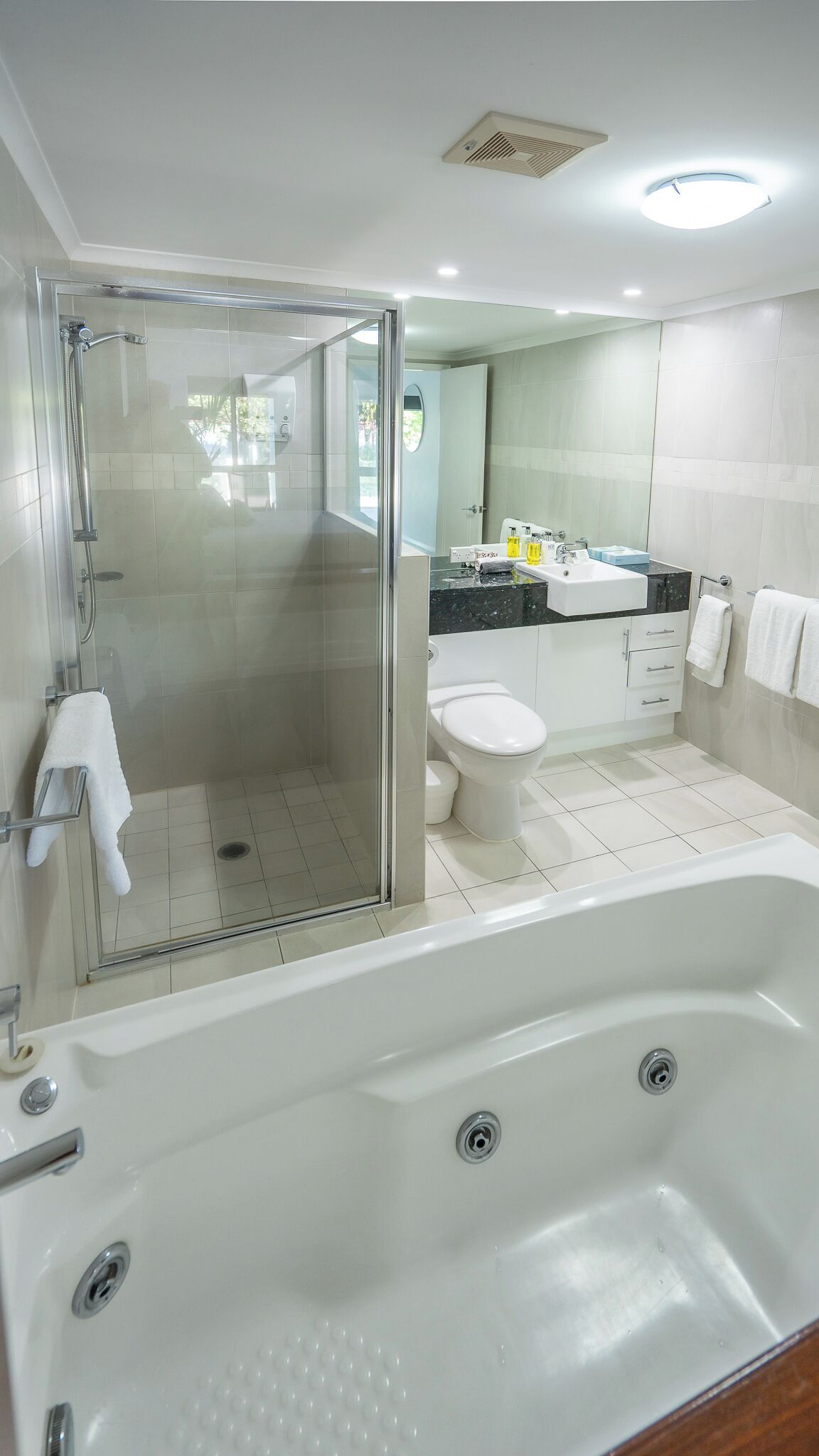 A modern bathroom with a glass-enclosed shower, a white bathtub, a toilet, and a sink with a mirror above it.