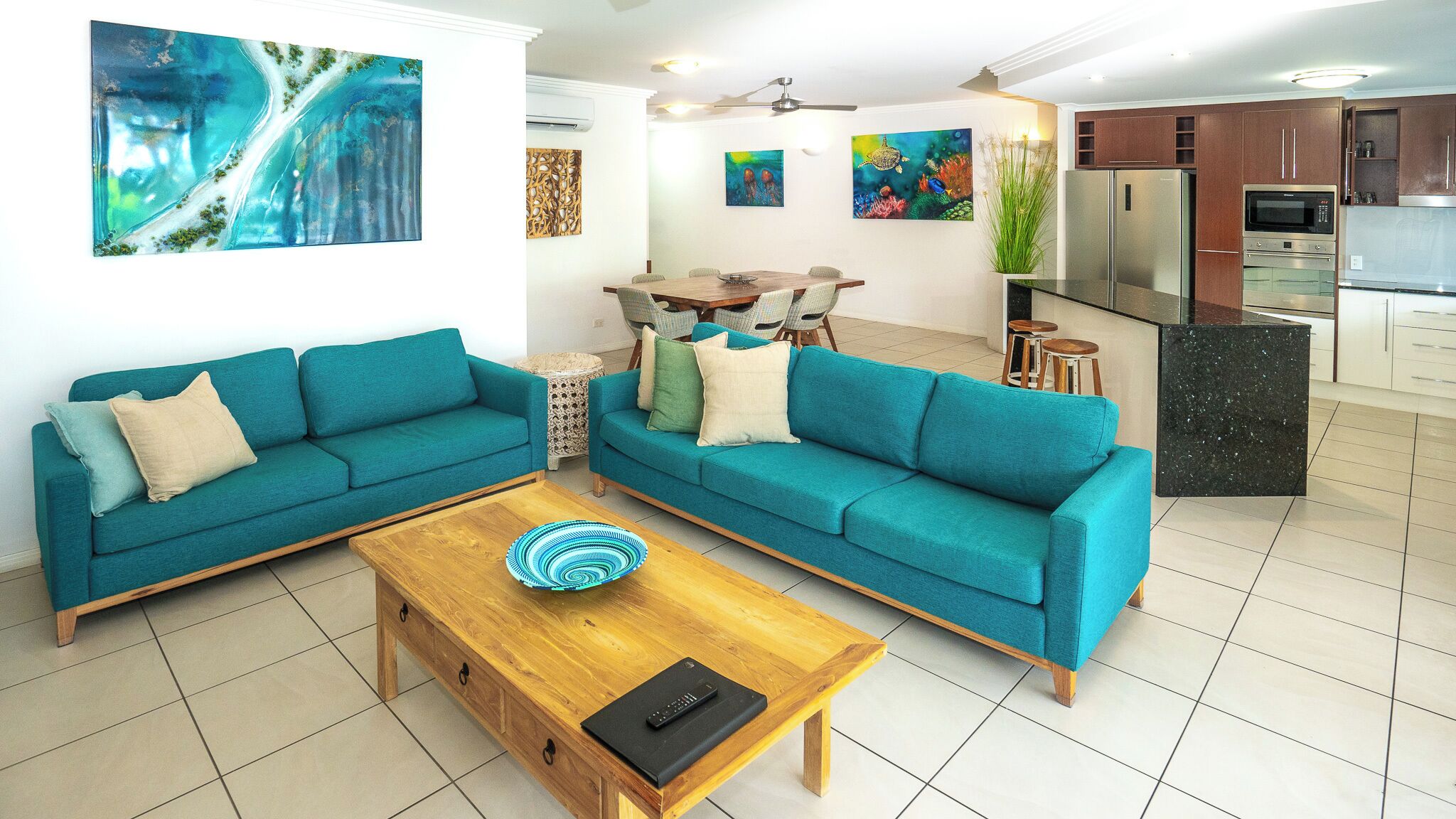 A living room with teal sofas, a wooden coffee table, and a dining area with a table and chairs.