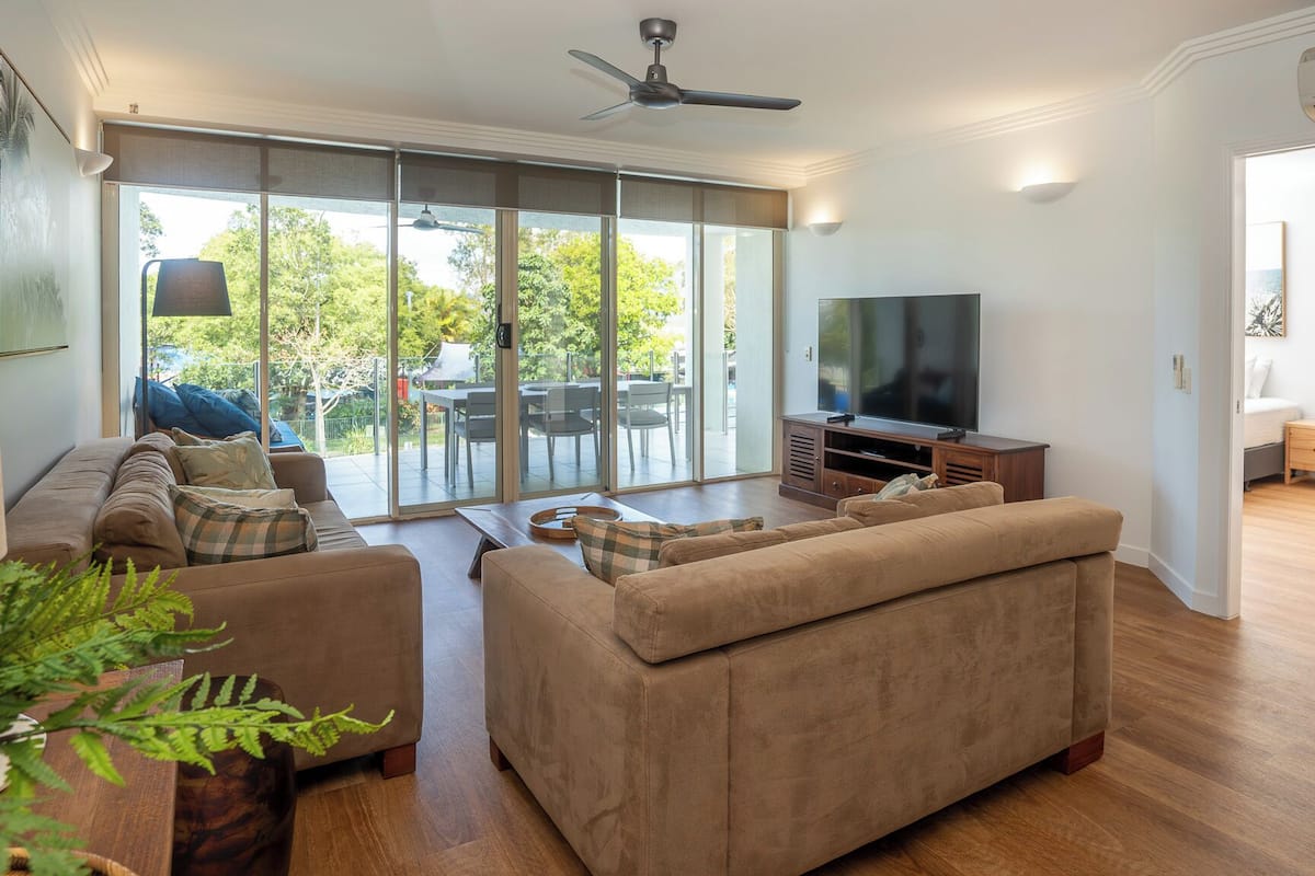 A modern living room with a large flat-screen TV, comfortable sofas, and a sliding glass door leading to a patio.