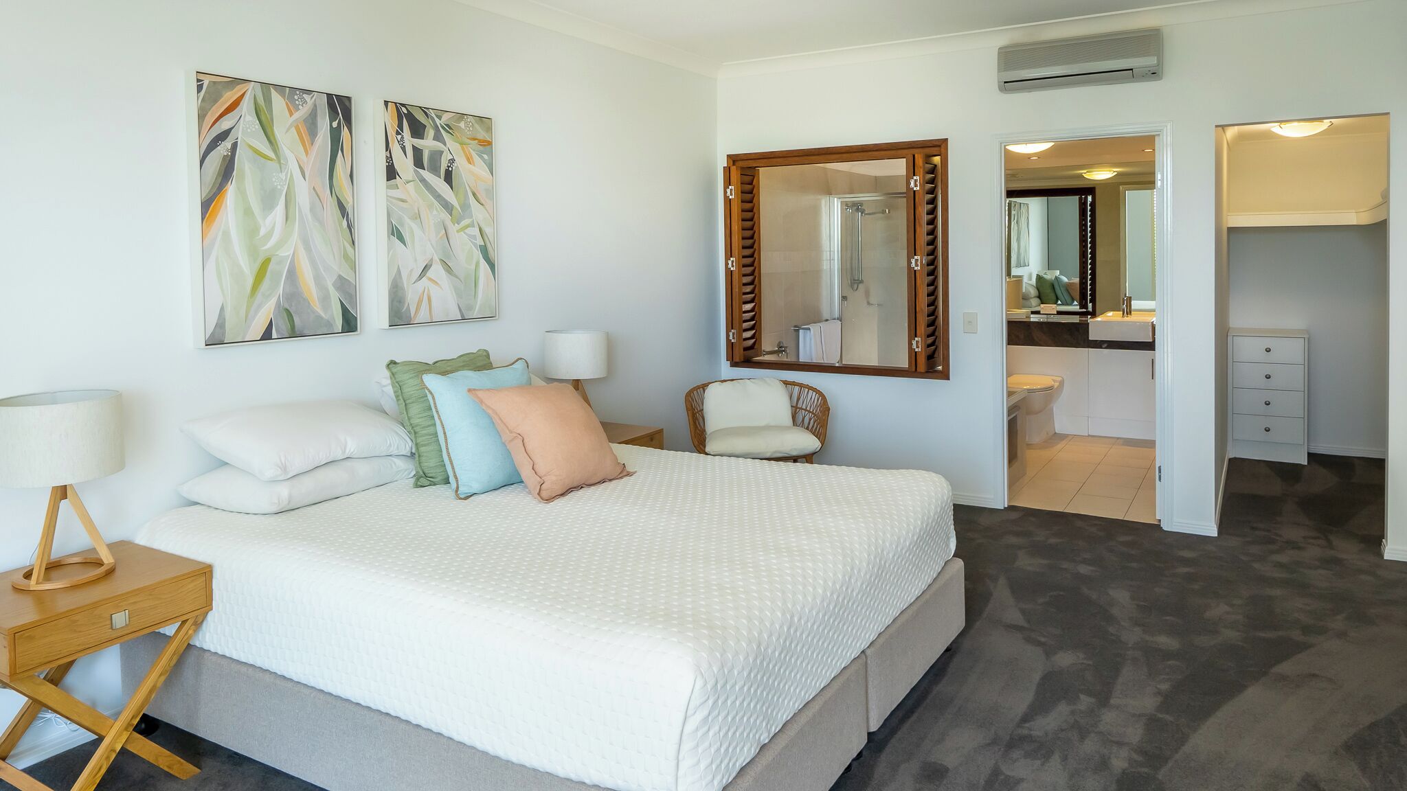A modern hotel room with a large bed, a bedside table with a lamp, a chair, and a bathroom visible through an open door.