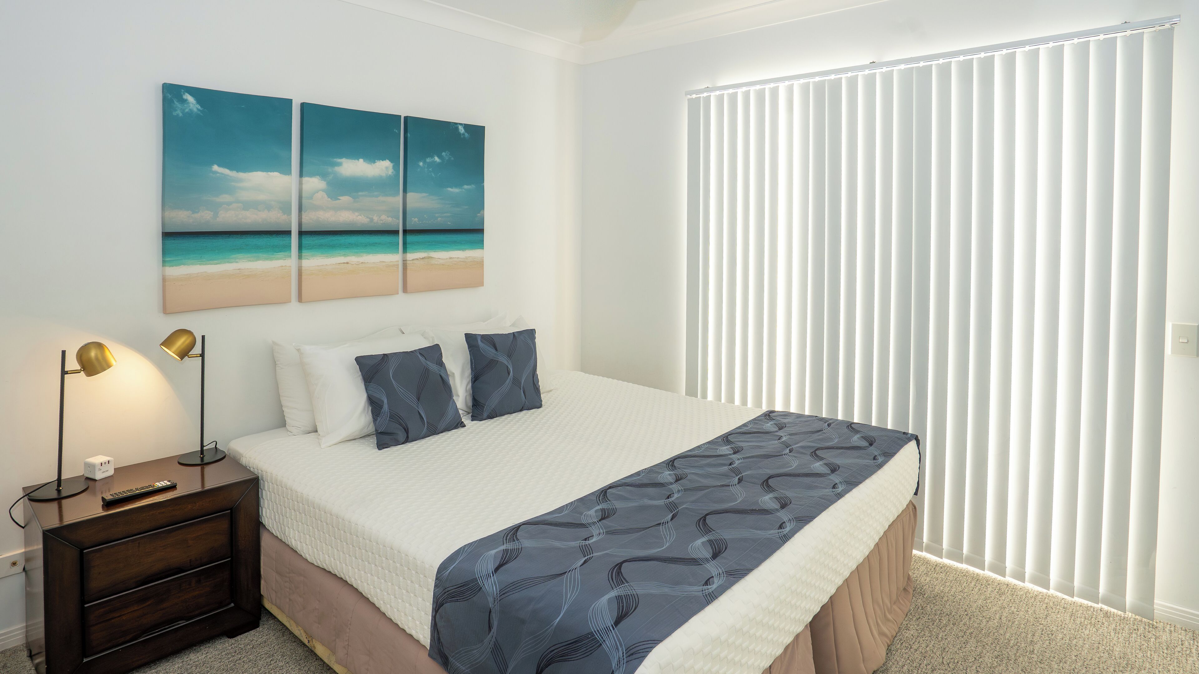 A bedroom with a bed, bedside lamps, a nightstand, and a window with blinds.