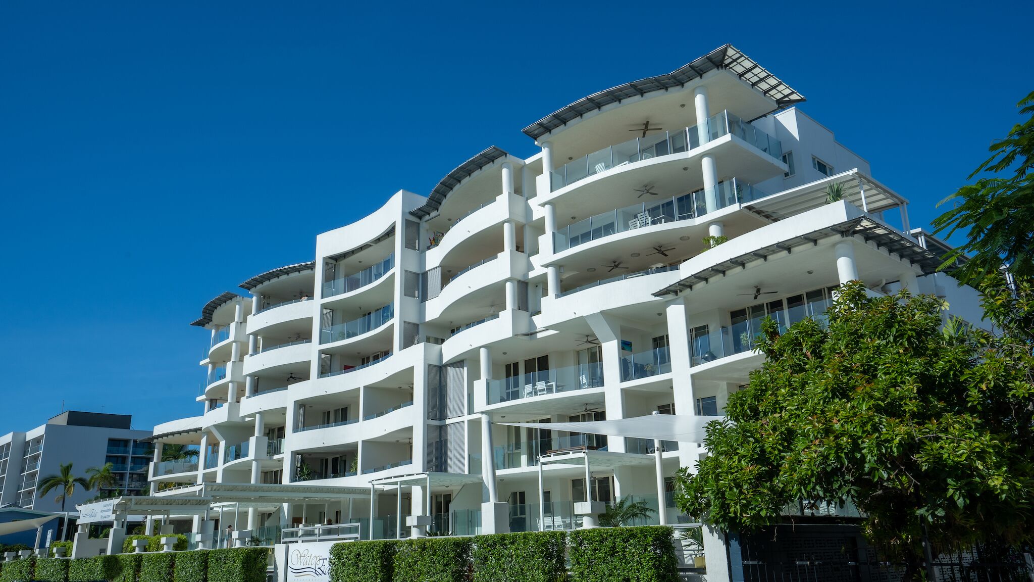 Un hotel de varios pisos con balcones, un espacio al aire libre cubierto y un cielo azul despejado.