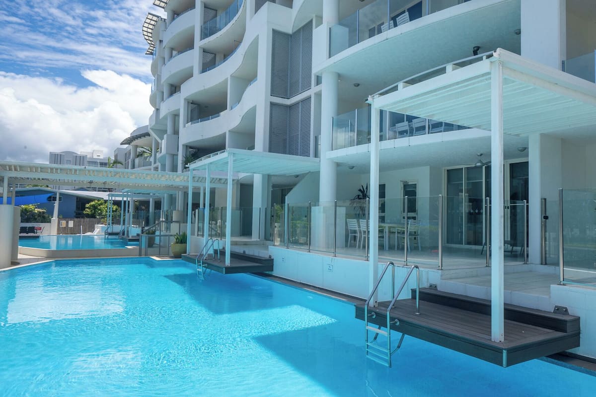A modern hotel with a large outdoor swimming pool, multiple balconies, and a covered seating area.