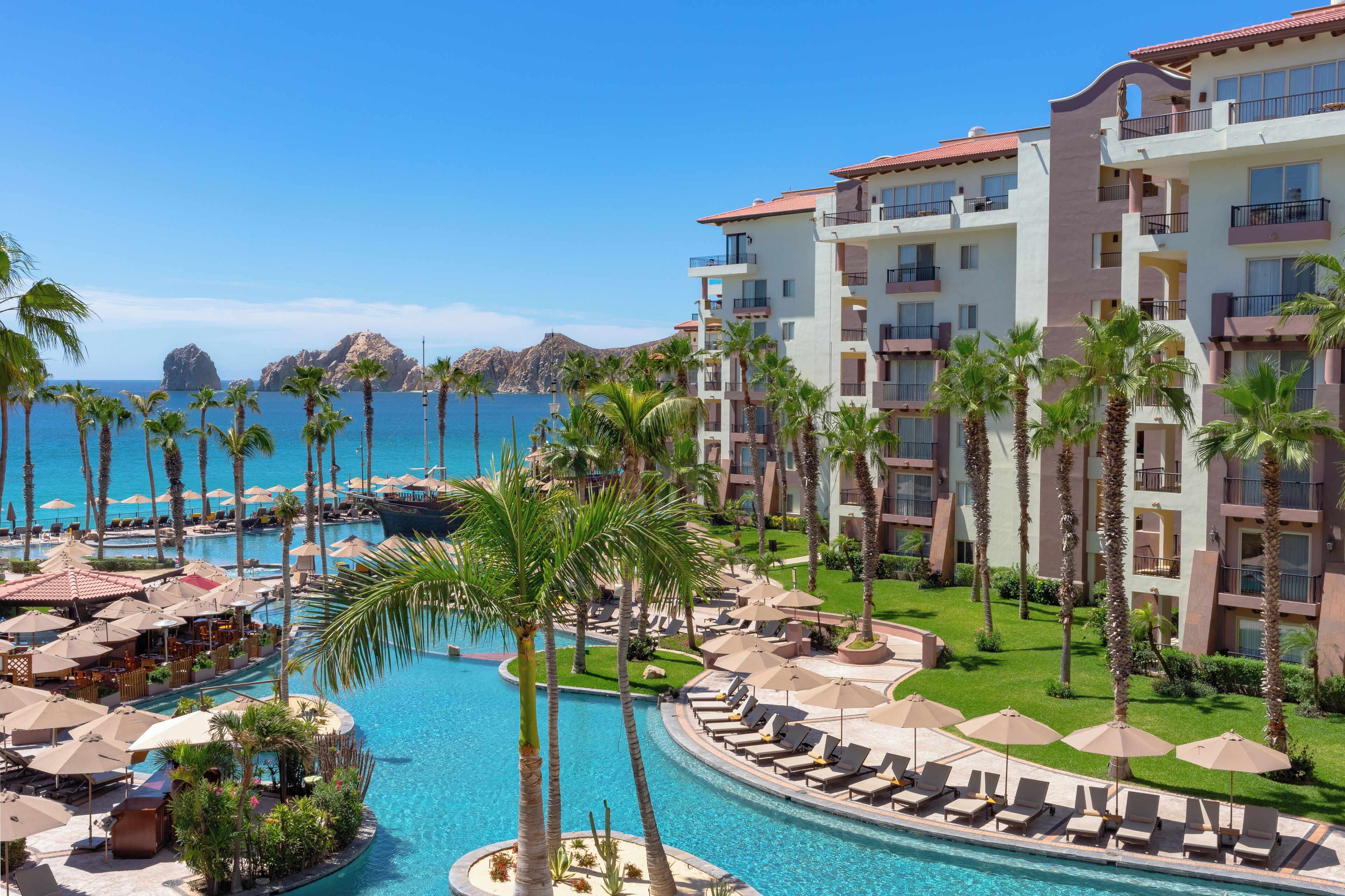 A resort with a swimming pool, palm trees, and a view of the ocean.
