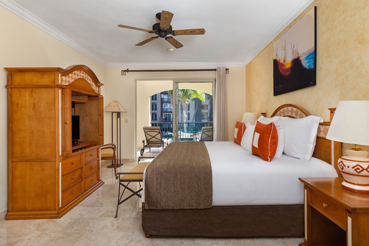 Habitación de hotel con una cama, un armario de madera, un ventilador de techo, un escritorio, una silla y vistas al exterior.