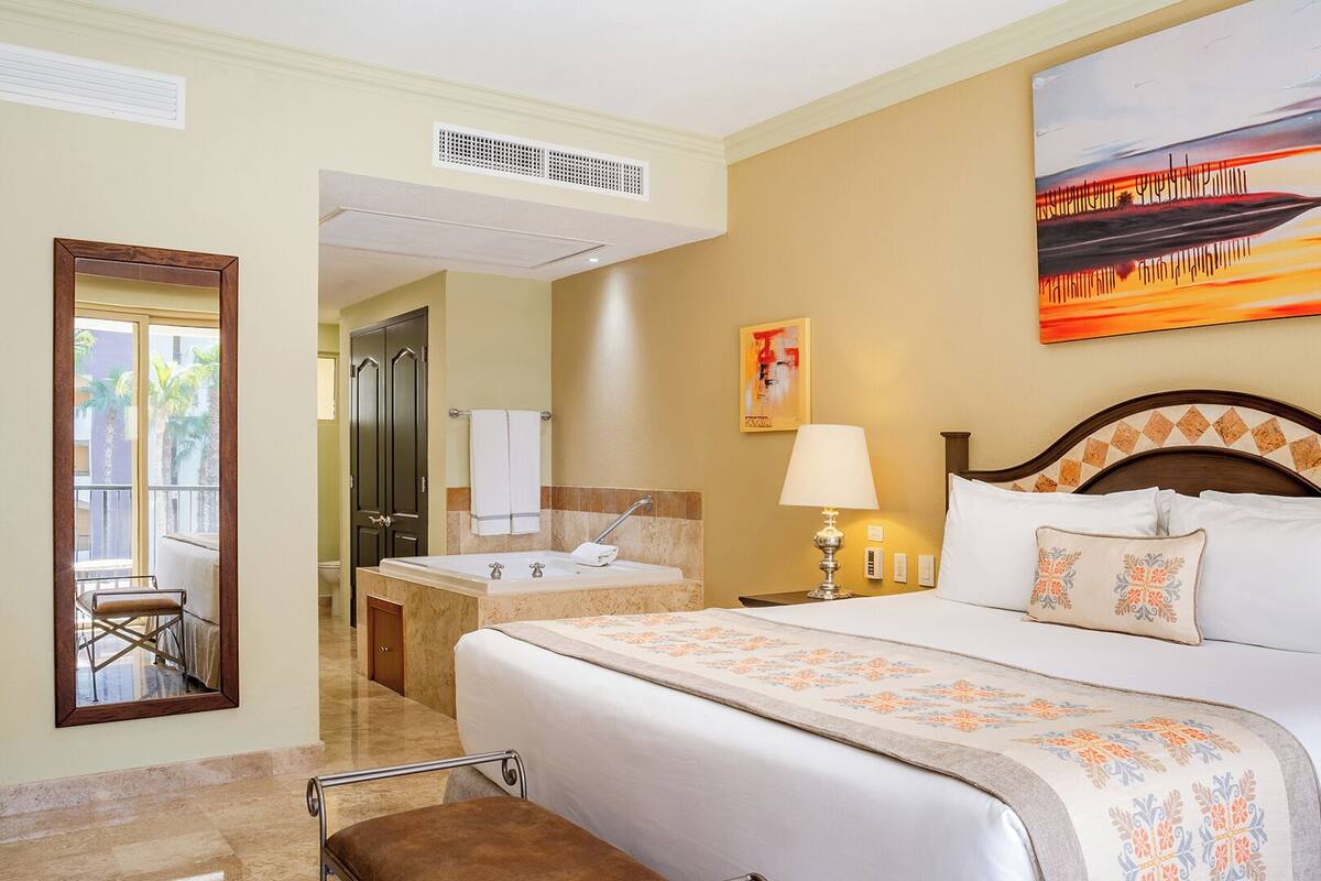 Habitación de hotel con cama, baño, zona de estar con una silla y un cuadro en la pared.