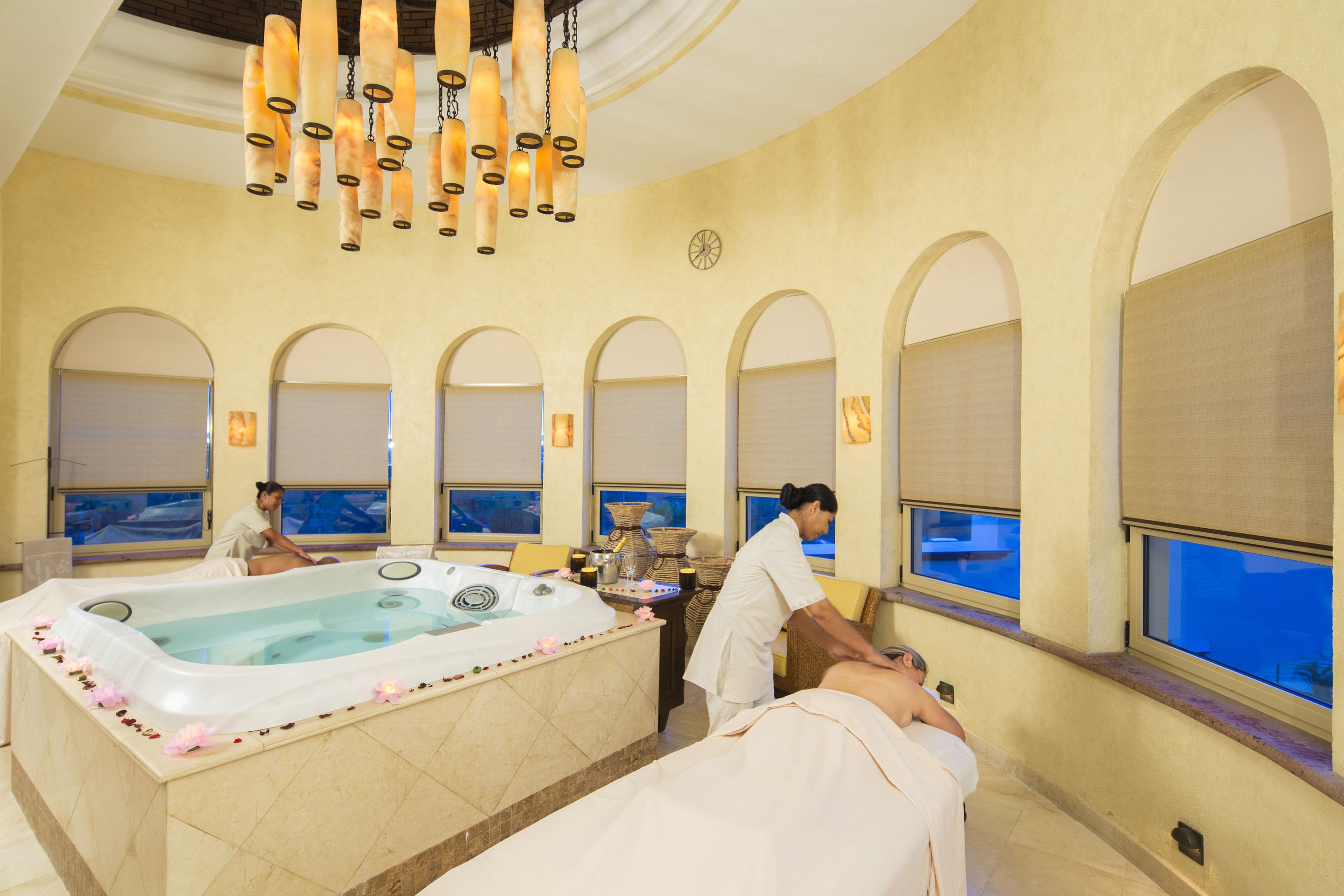 A spa room with a large bathtub, a massage table, and a person receiving a massage.