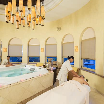 A spa room with a large bathtub, a massage table, and a person receiving a massage.