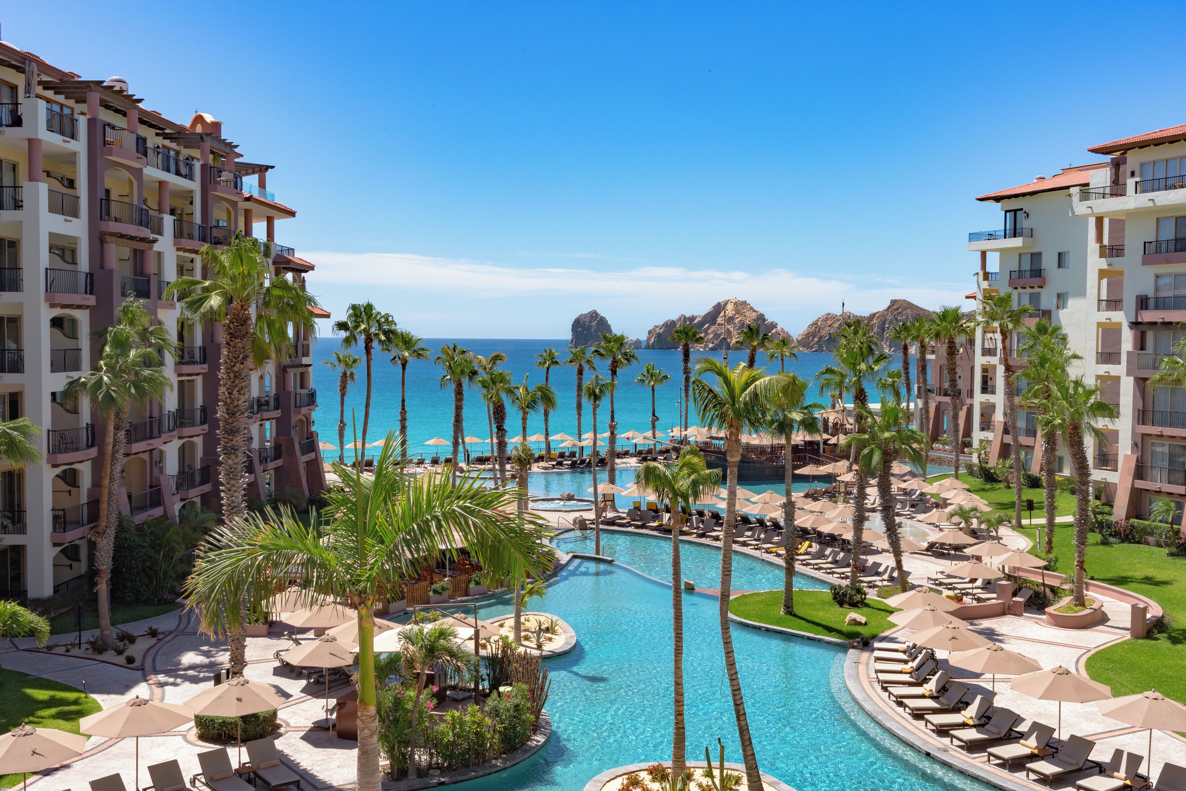 A resort with multiple swimming pools, palm trees, and a view of the ocean.