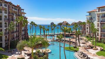 A resort with multiple swimming pools, palm trees, and a view of the ocean.