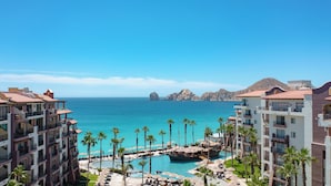 Un resort con varios balcones, una piscina central y vistas al mar y formaciones rocosas.