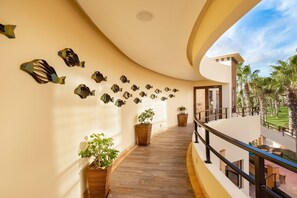 A curved balcony with a wooden floor, potted plants, and a view of palm trees.