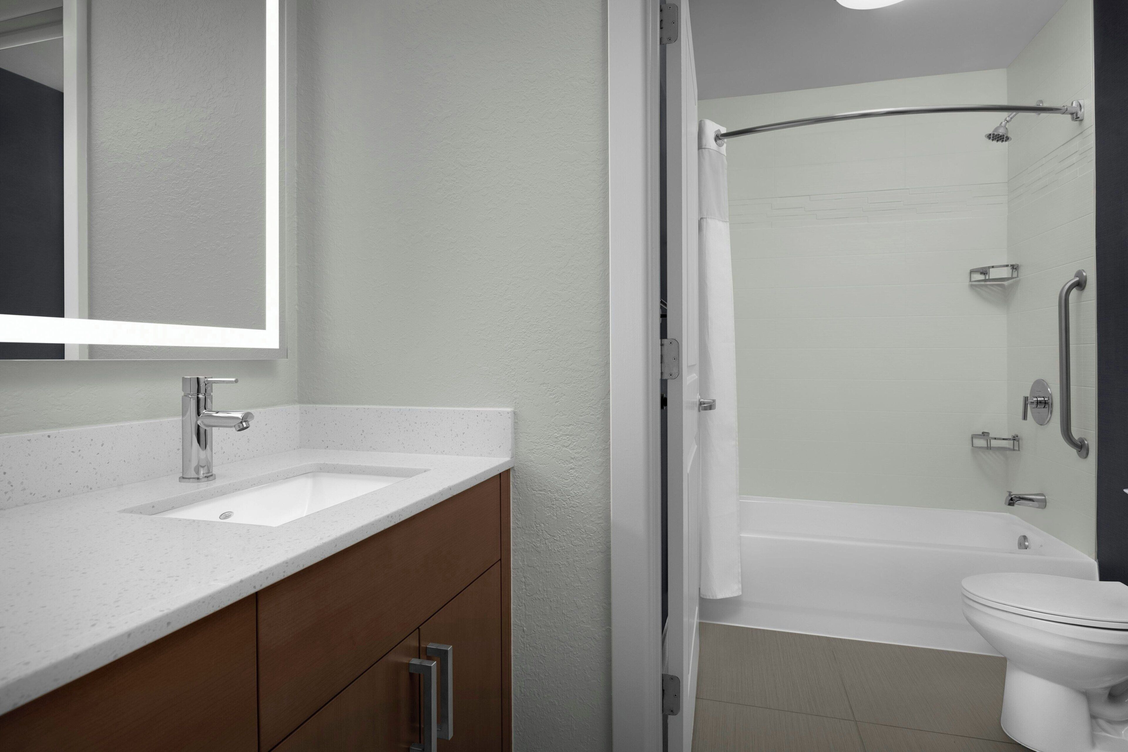 A bathroom with a white sink, mirror, and toilet, a shower area, and a bathtub.