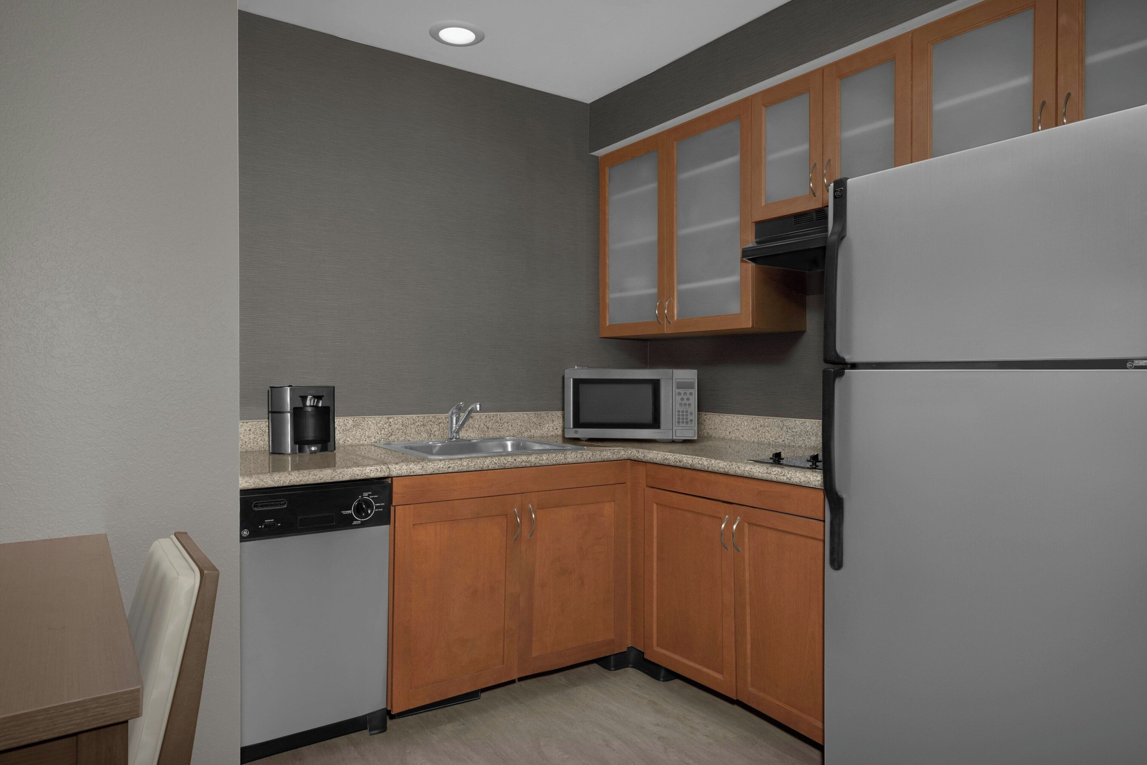 Cocina compacta con armarios de madera, un microondas, un lavavajillas y un refrigerador.