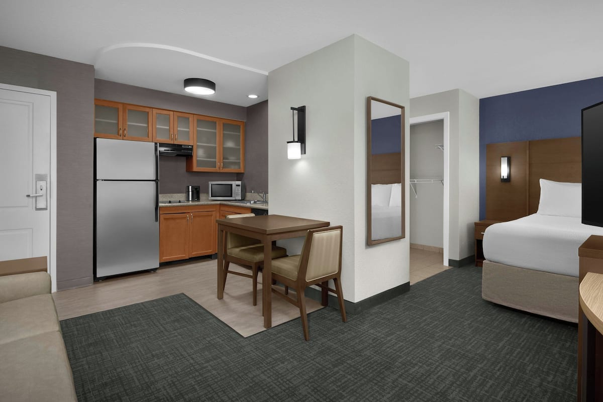 A hotel room with a kitchenette, a bed, a desk, and a chair.