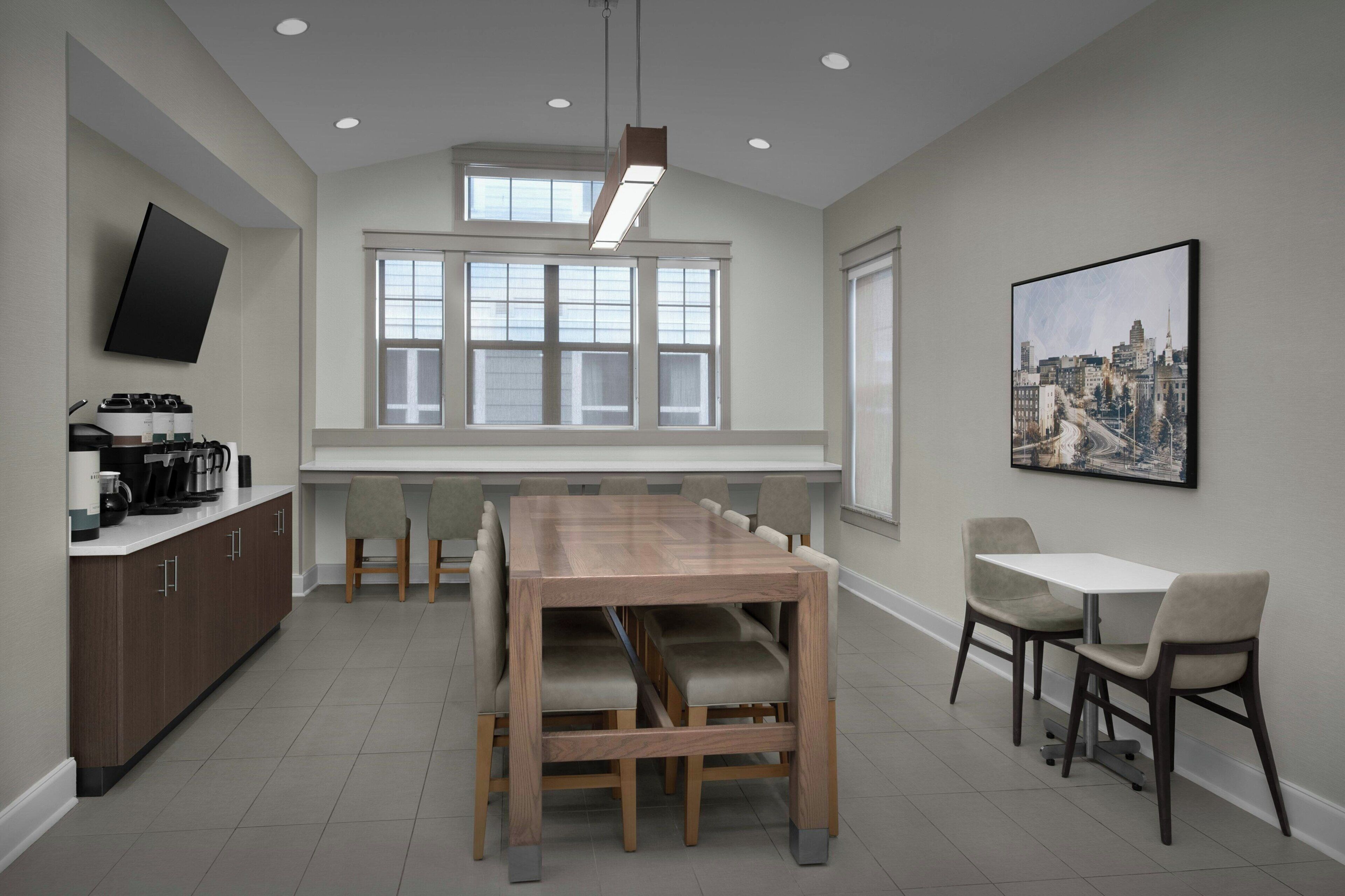 A modern kitchen with a dining area, large windows, and a cityscape painting.