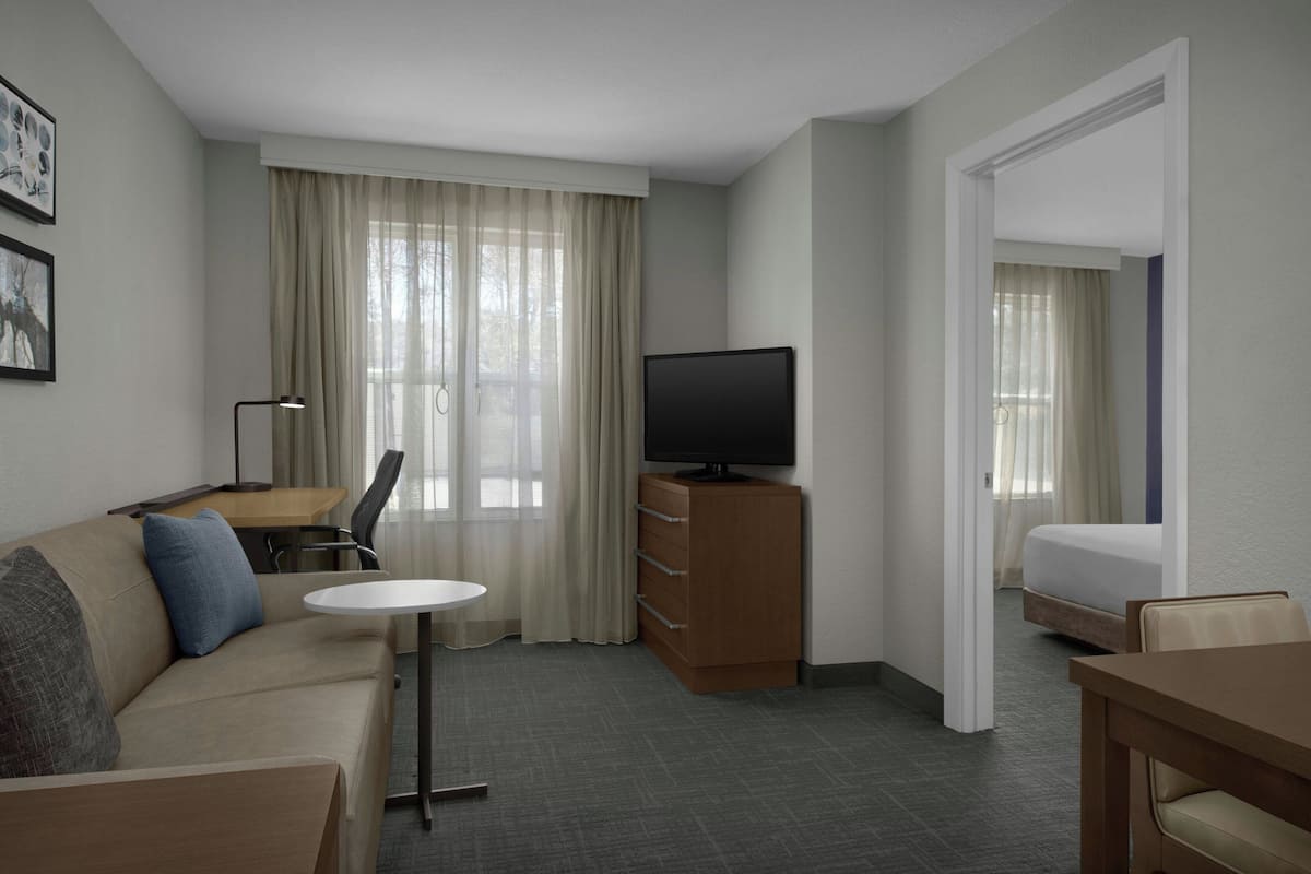 A hotel room with a sofa, a TV on a wooden cabinet, a small table, a desk, and a bed.