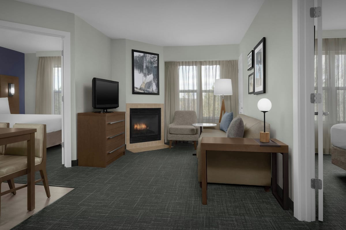 A hotel room with a bed, a desk, a television, a fireplace, a sofa, and a lamp.