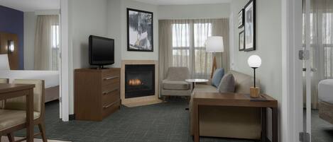 A hotel room with a bed, a desk, a television, a fireplace, a sofa, and a lamp.
