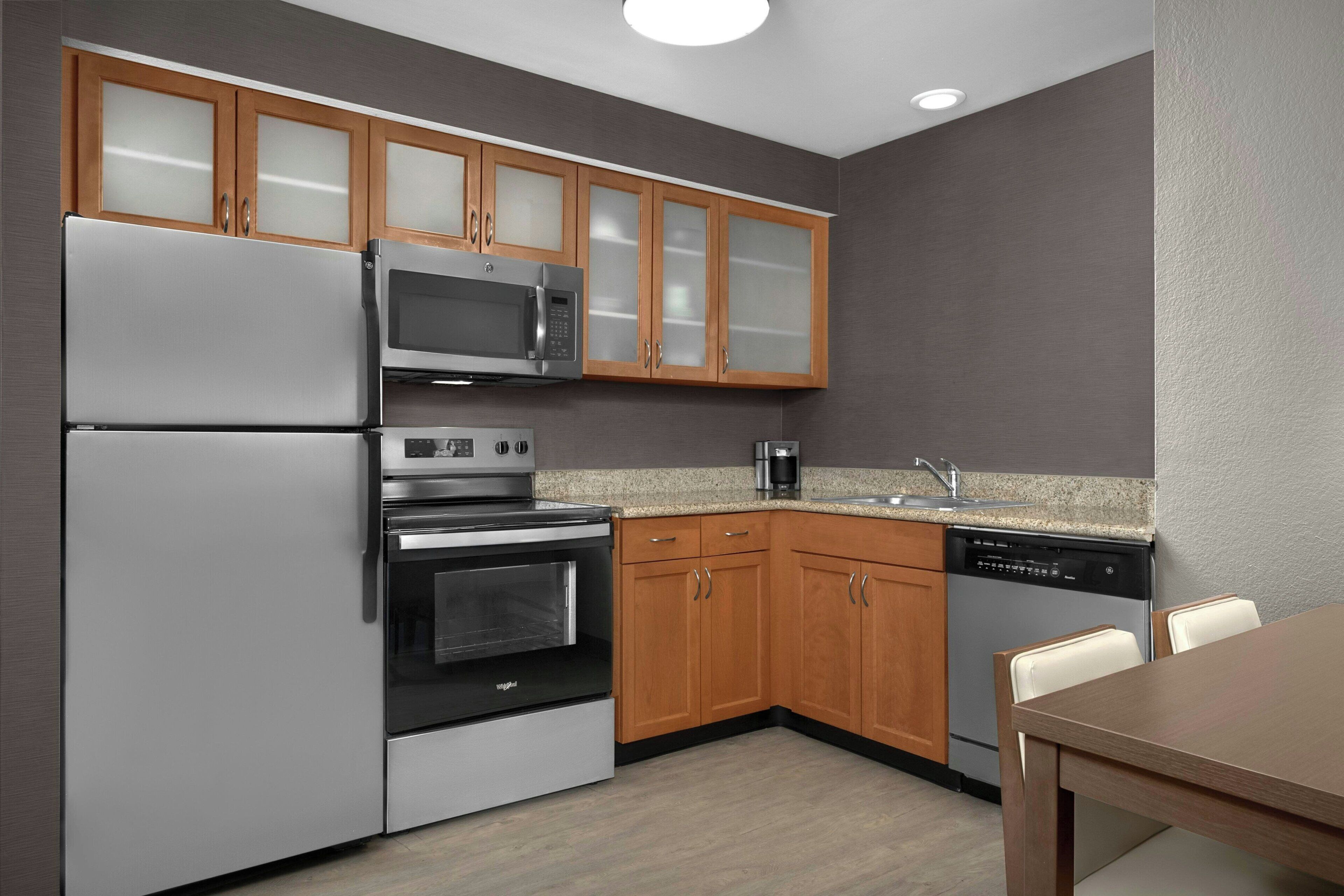 A modern kitchen with stainless steel appliances, wooden cabinets, and a granite countertop.