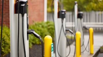 A row of electric vehicle charging stations with yellow bollards, connected to the ground by cables.